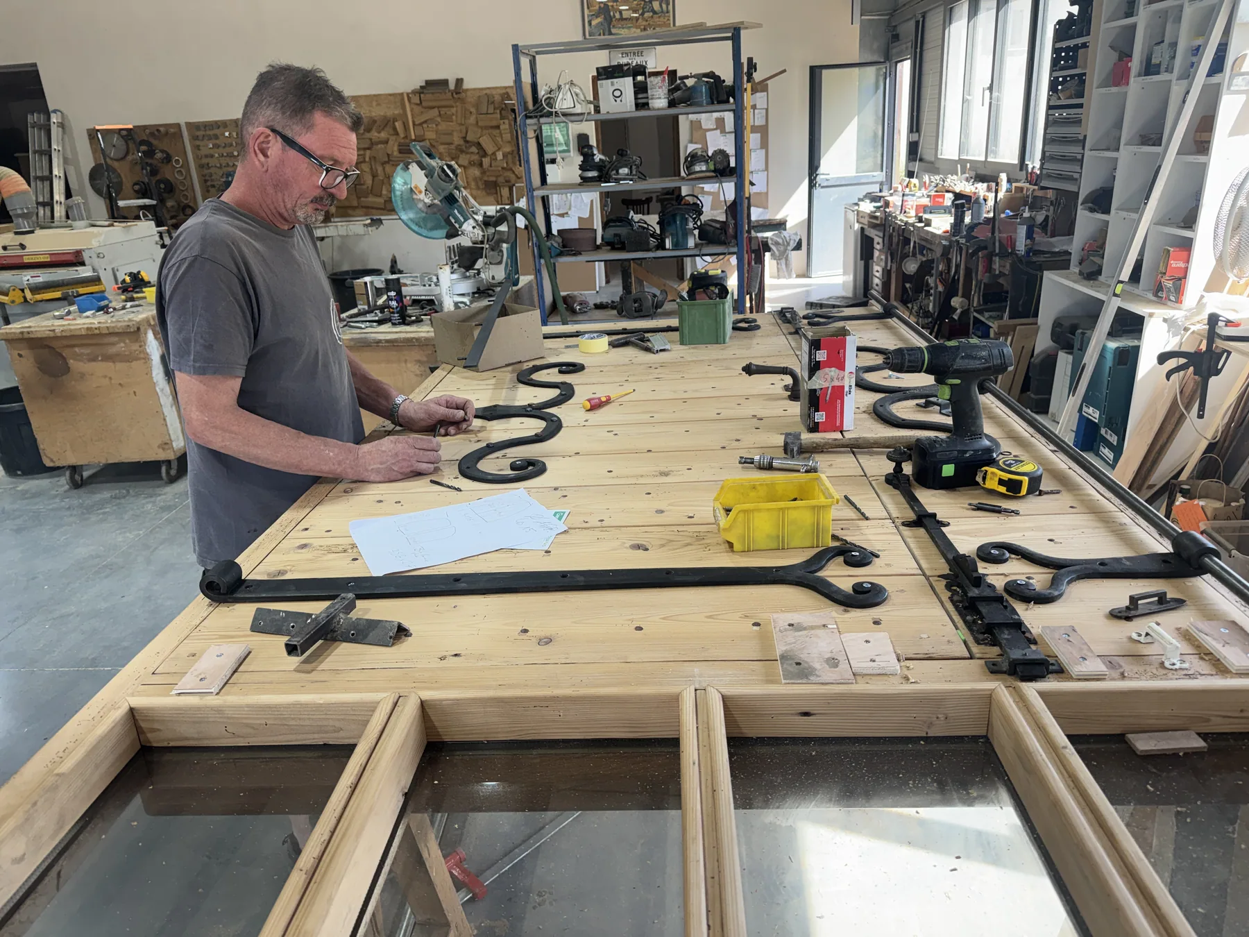 Un artisan pose des ferrures forgées sur une grande porte en cours de fabrication à l'atelier d'Eygalières