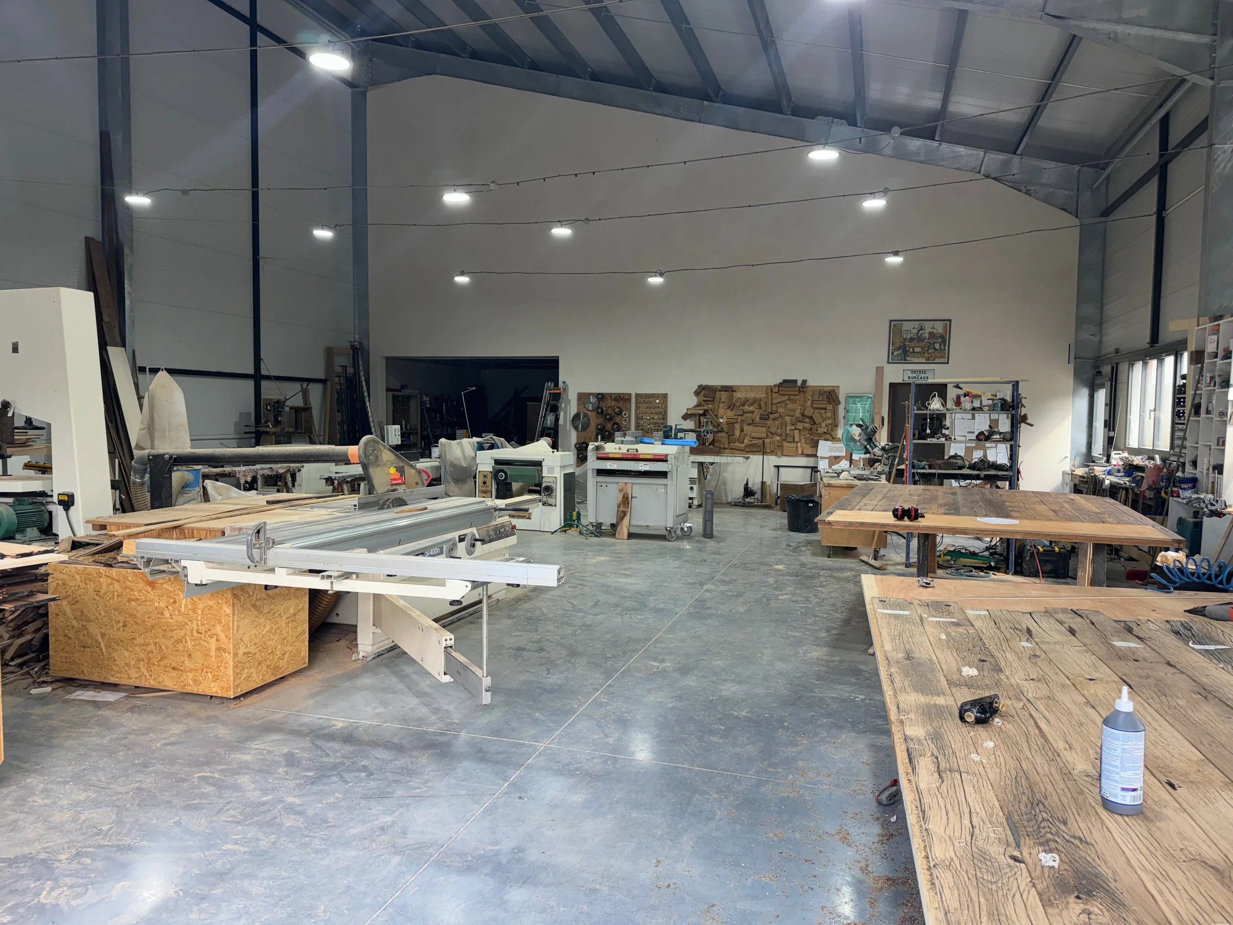 Intérieur de l'atelier d'Esprit Vieux Bois à Eygalières : scie à format, établis et plateaux en vieux chêne