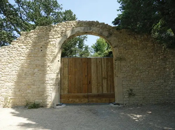 Portail en vieux pin sous une arche de pierre sèche, ferronnerie ancienne